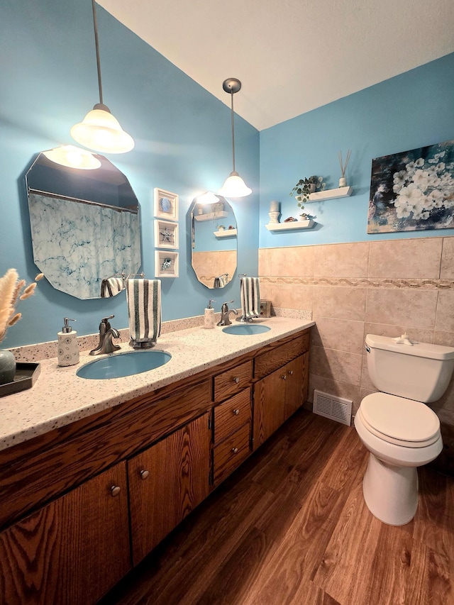 full bathroom featuring tile walls, toilet, wood finished floors, double vanity, and wainscoting