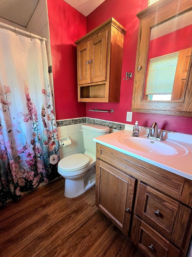 full bath featuring tile walls, wood finished floors, toilet, vanity, and a wainscoted wall