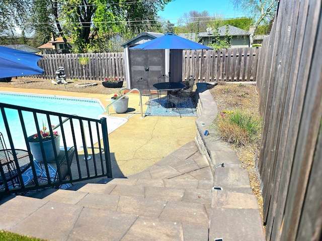 view of pool with a patio area, a fenced backyard, an outdoor structure, and a storage unit