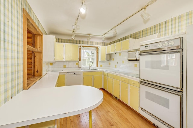 kitchen featuring white appliances, wallpapered walls, light wood finished floors, a sink, and light countertops