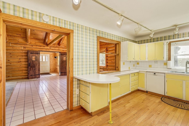 kitchen with dishwasher, a sink, light countertops, wallpapered walls, and light wood finished floors