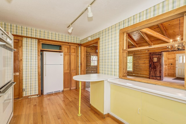kitchen with wallpapered walls, freestanding refrigerator, light wood-style floors, light countertops, and a chandelier