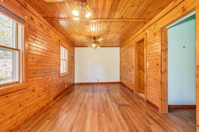 empty room with wood walls, wood ceiling, light wood-style floors, baseboards, and ceiling fan