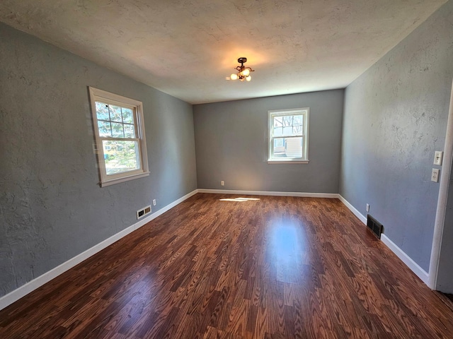 spare room featuring wood finished floors, a textured wall, and baseboards