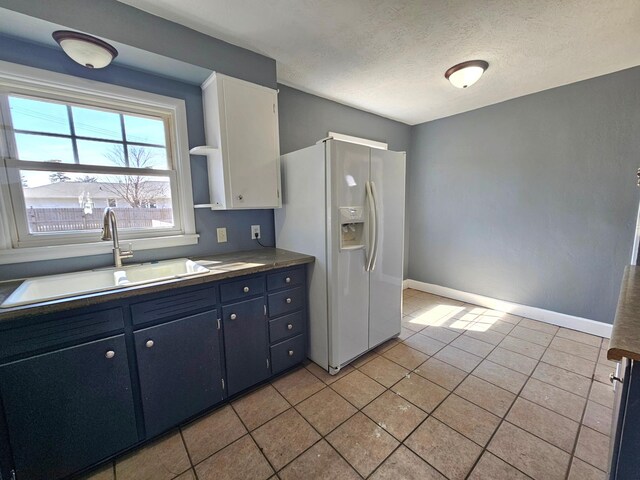 kitchen with a sink, white fridge with ice dispenser, light tile patterned flooring, a textured ceiling, and baseboards
