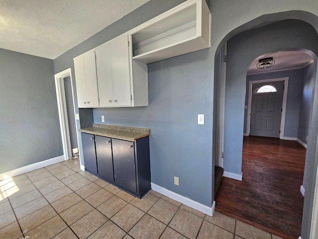 kitchen with arched walkways, white cabinetry, baseboards, light tile patterned floors, and a textured ceiling