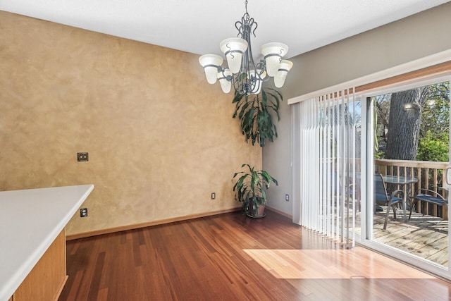 unfurnished dining area with dark wood-type flooring, a chandelier, and baseboards