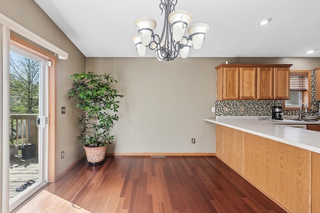 kitchen featuring backsplash, light countertops, wood finished floors, a chandelier, and baseboards