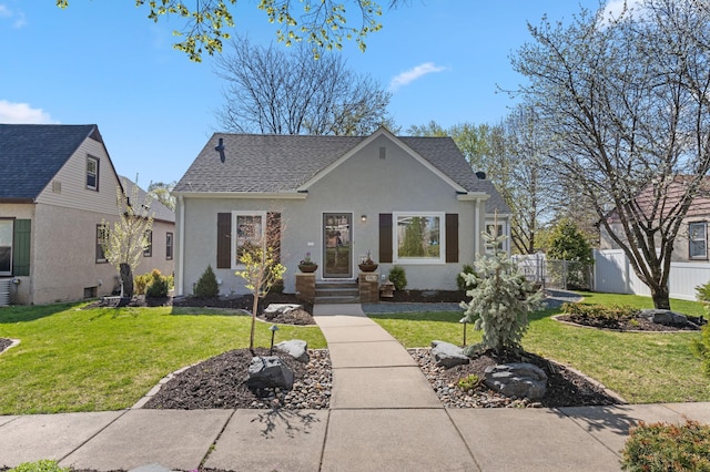 view of front of house featuring roof with shingles, fence, and a front yard