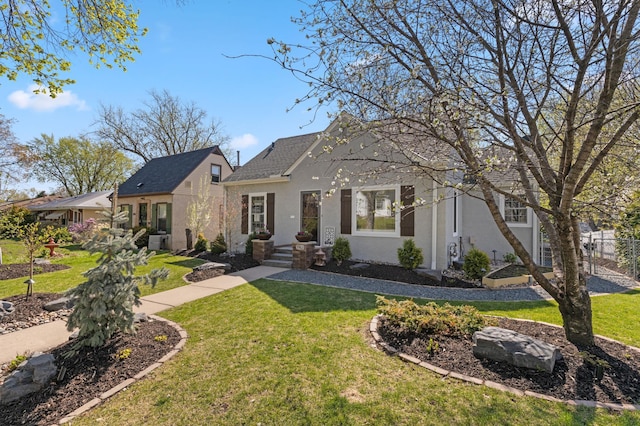 view of front facade with a front yard, stucco siding, and roof with shingles