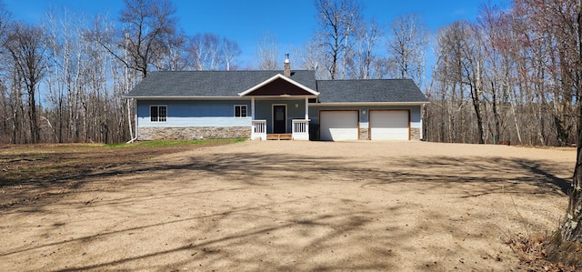 view of front of house featuring roof with shingles, an attached garage, stone siding, a chimney, and dirt driveway