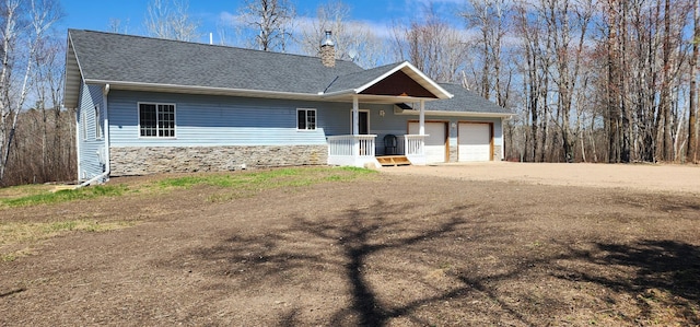 view of front of home with an attached garage, stone siding, a chimney, a shingled roof, and driveway
