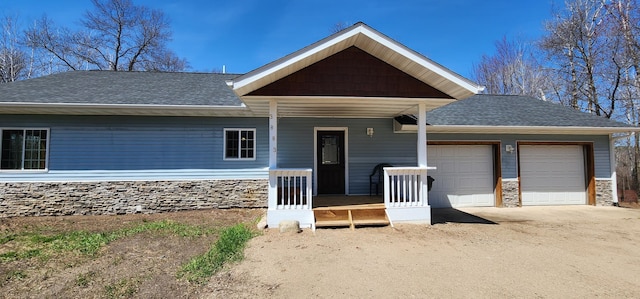 view of front of property with a porch, roof with shingles, stone siding, driveway, and a garage