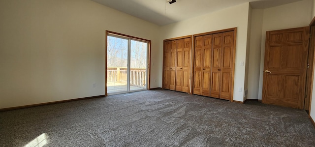 unfurnished bedroom featuring baseboards, dark carpet, multiple closets, and access to exterior