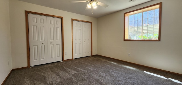 unfurnished bedroom with baseboards, dark carpet, and multiple closets
