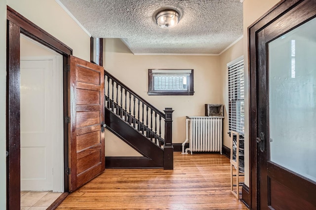 entryway with radiator heating unit, crown molding, a textured ceiling, and wood finished floors