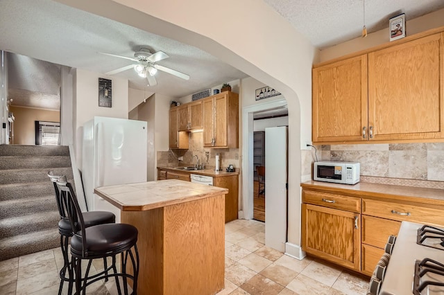 kitchen featuring white appliances, tasteful backsplash, a breakfast bar, a textured ceiling, and a kitchen island