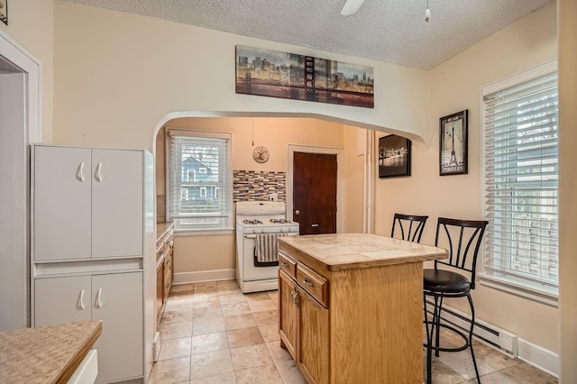 kitchen with a breakfast bar area, a center island, a baseboard heating unit, white gas range oven, and arched walkways