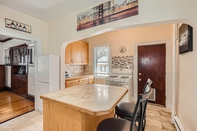 kitchen featuring white range with gas cooktop, tile countertops, backsplash, arched walkways, and baseboard heating