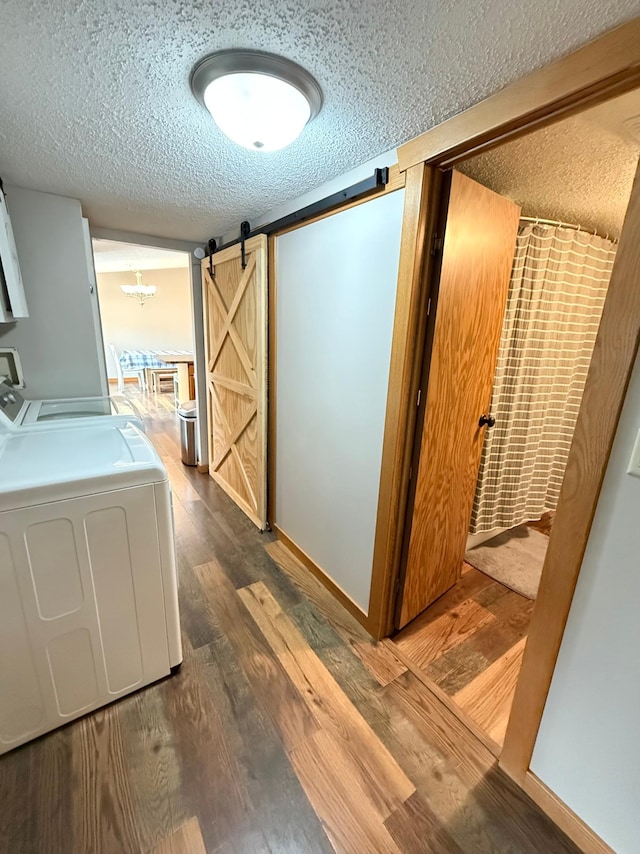 laundry room featuring a barn door, a textured ceiling, washer and clothes dryer, wood finished floors, and baseboards