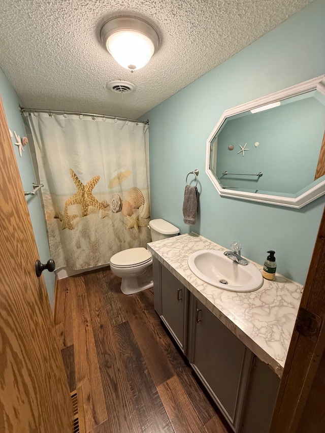 full bathroom featuring wood finished floors, a textured ceiling, vanity, toilet, and curtained shower