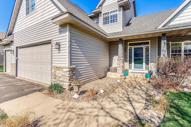 1103 Park Ln SE, New Prague, MN 56071 - doorway to property featuring a shingled roof, stone siding, driveway, a garage, and covered porch