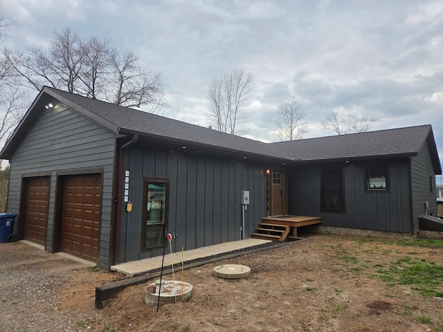 view of side of home featuring a garage, dirt driveway, board and batten siding, and a shingled roof