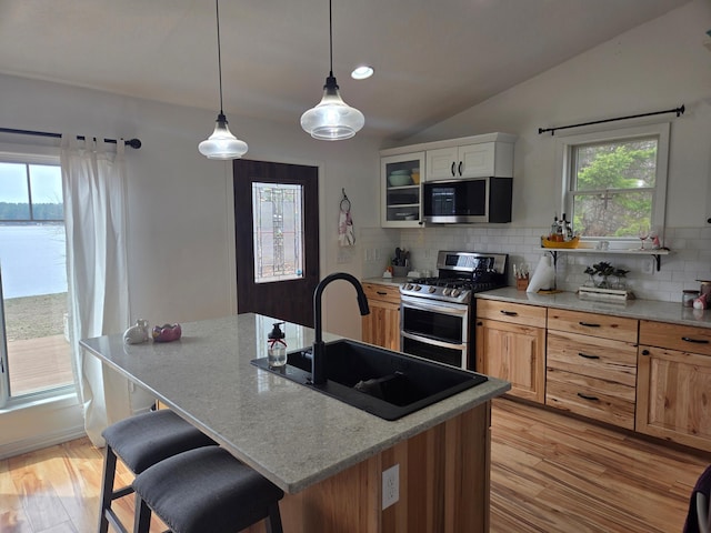 kitchen with appliances with stainless steel finishes, a sink, tasteful backsplash, light wood-style flooring, and vaulted ceiling