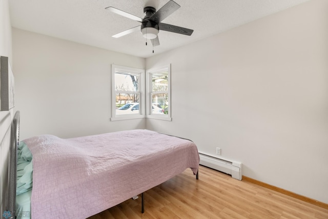 bedroom featuring baseboard heating, light wood-type flooring, baseboards, and a ceiling fan