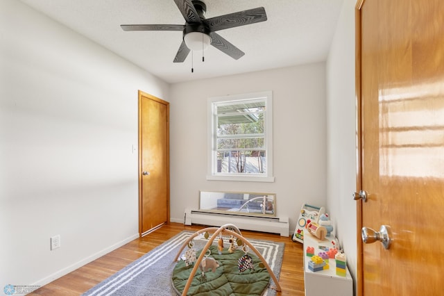 recreation room with a baseboard radiator, ceiling fan, wood finished floors, and baseboards