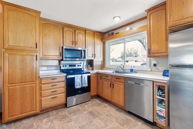 kitchen featuring appliances with stainless steel finishes, a sink, light countertops, a textured ceiling, and stone finish flooring