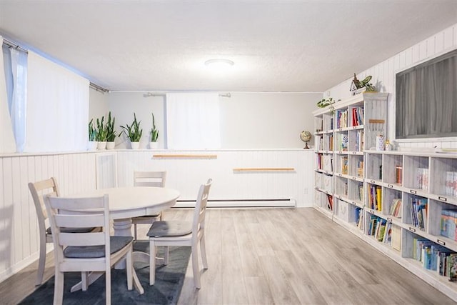 dining room with baseboard heating, wainscoting, wood walls, and wood finished floors