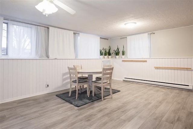 dining area with wood finished floors, a wainscoted wall, baseboard heating, ceiling fan, and wooden walls