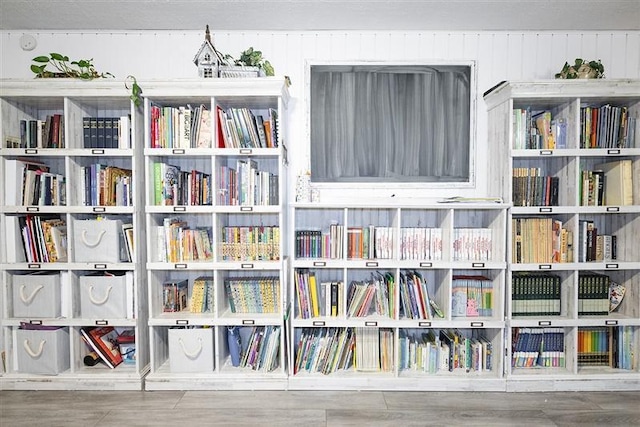 unfurnished room with wall of books and wood finished floors