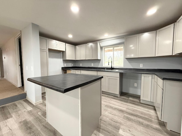 kitchen featuring a sink, recessed lighting, dark countertops, and light wood-style floors