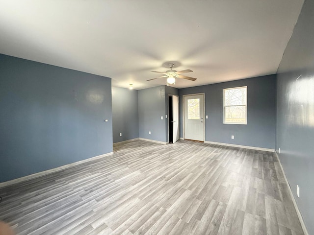 empty room featuring a ceiling fan, baseboards, and light wood-style flooring