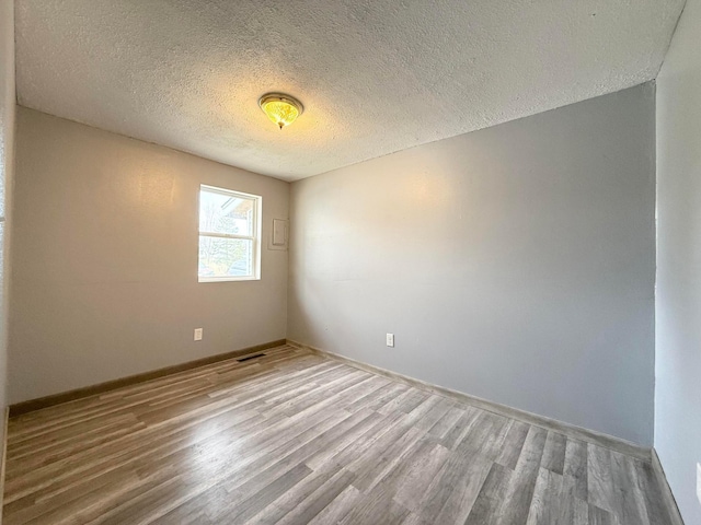 unfurnished room with a textured ceiling, visible vents, wood finished floors, and baseboards