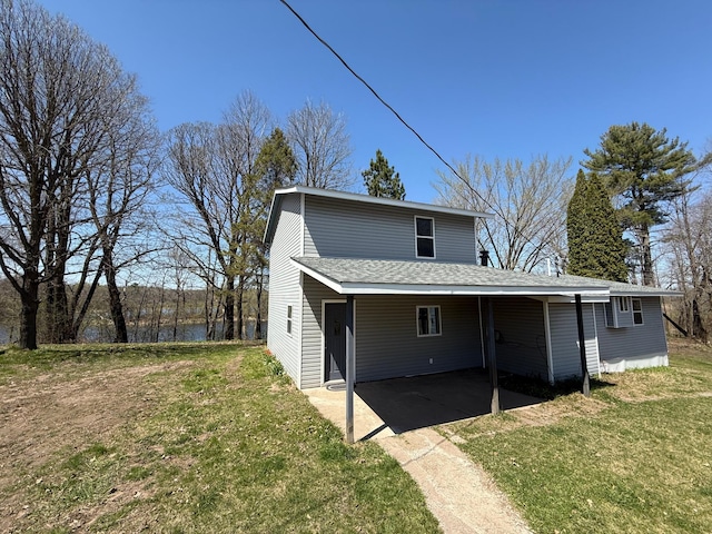 back of house featuring concrete driveway, an attached carport, roof with shingles, and a lawn
