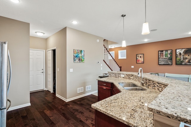 kitchen featuring a sink, freestanding refrigerator, dark wood-style floors, baseboards, and pendant lighting