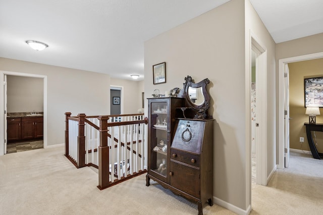 hall featuring an upstairs landing, light colored carpet, and baseboards