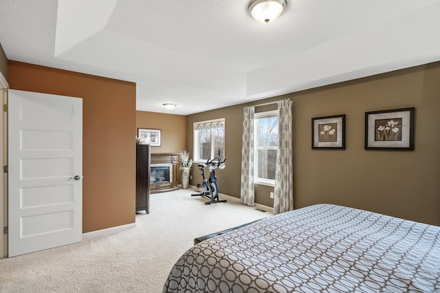 carpeted bedroom featuring a glass covered fireplace and baseboards
