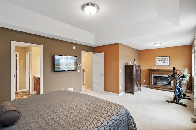 bedroom featuring a glass covered fireplace, a raised ceiling, light carpet, and baseboards