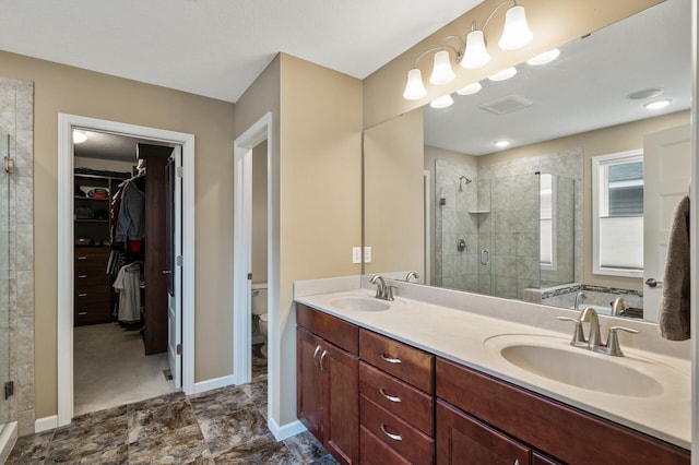bathroom with a shower stall, toilet, a walk in closet, double vanity, and baseboards