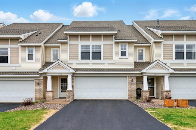 view of property featuring roof with shingles, driveway, brick siding, and a garage