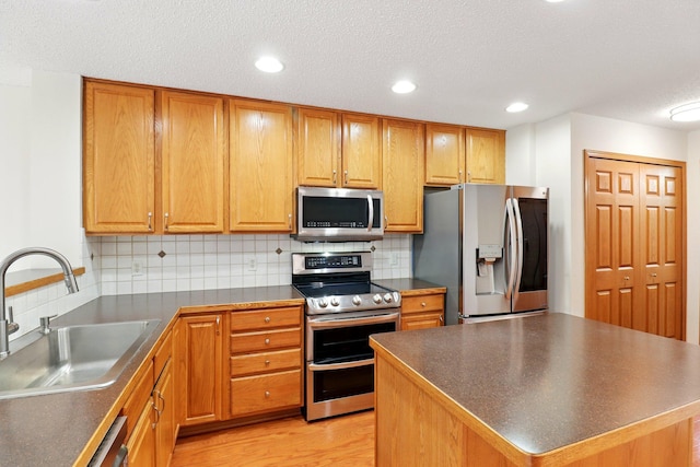 kitchen with appliances with stainless steel finishes, a sink, dark countertops, tasteful backsplash, and light wood-type flooring