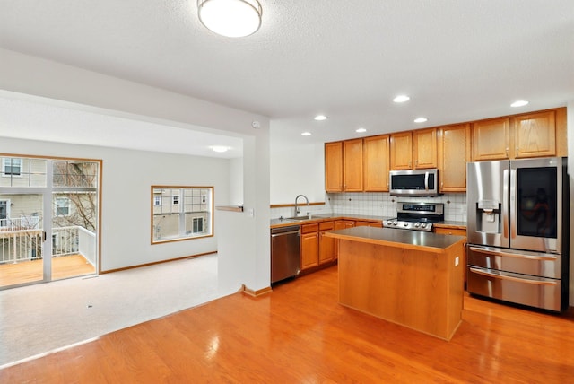 kitchen featuring a center island, a sink, light wood-type flooring, backsplash, and appliances with stainless steel finishes