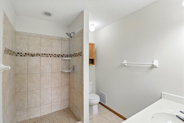 bathroom featuring toilet, a tile shower, a sink, tile patterned floors, and visible vents