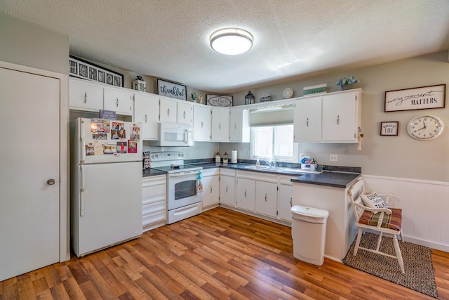 kitchen featuring white appliances, dark countertops, light wood finished floors, white cabinetry, and a textured ceiling