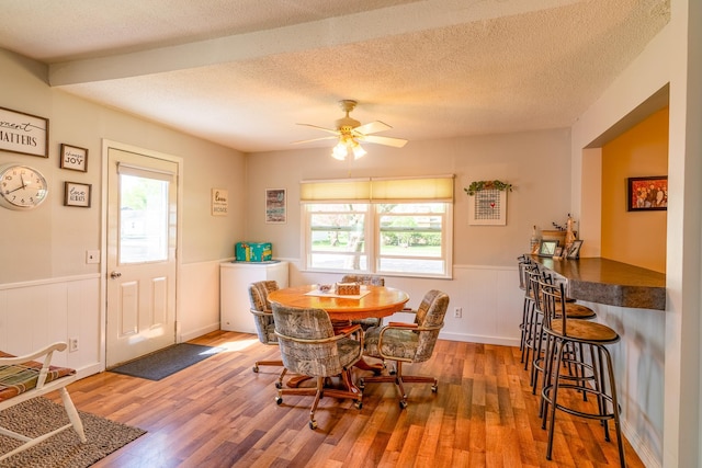 dining space with healthy amount of natural light, a wainscoted wall, wood finished floors, a ceiling fan, and a textured ceiling