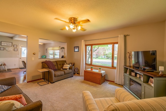 living room featuring a ceiling fan, light colored carpet, and a textured ceiling